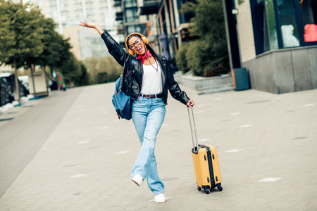 Young stylish woman pulling yellow suitcase on city street during leisure travel, expressing happiness and joyの写真素材