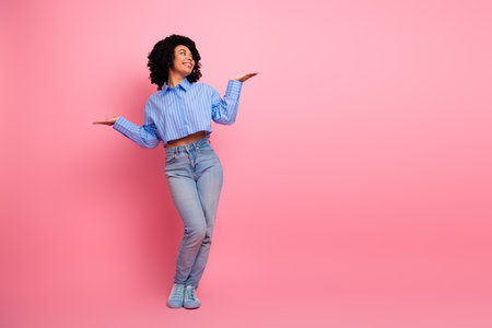 Cheerful woman gesturing with open arms on pink background wearing casual outfit expressing positivity and confidenceの写真素材