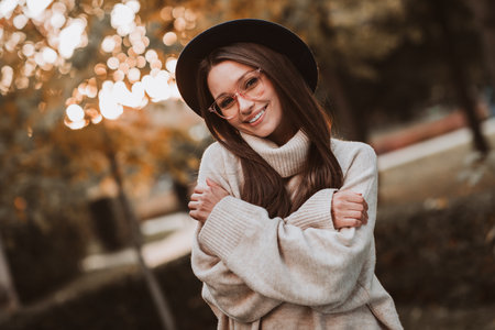 Charming young woman enjoys a sunny autumn day outdoors wearing a stylish hat and sweater in warm golden lightの写真素材