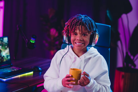Teen boy smiling while engaging in video streaming activities with vibrant neon light atmosphereの写真素材
