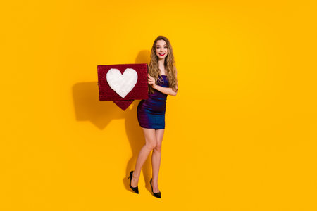 Stylish young woman holding a decorative heart box against a bright yellow background in a trendy and charming pose.の写真素材