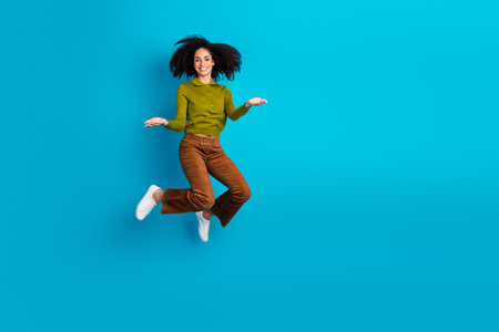 Energetic young woman in trendy casual outfit jumping with joy against a vibrant blue background showcasing her charmの写真素材