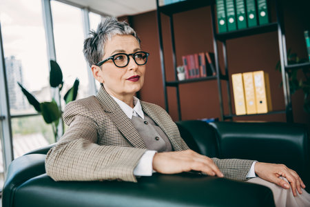 Confident businesswoman sitting in office interior wearing formal attire with a professional and poised presence and gazeの写真素材