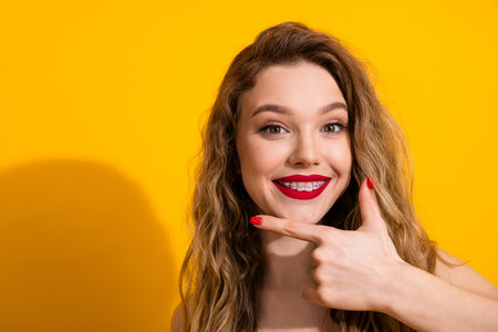 Young cheerful woman showing braces with smile and hand gesture against yellow background during leisure timeの写真素材