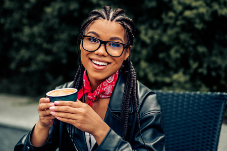 Young woman enjoying a cozy coffee moment outdoors with charming smile and relaxed style in an urban street settingの写真素材