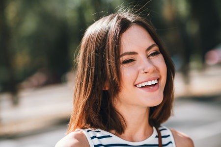 Young woman in striped shirt smiling joyfully outdoors on sunny day