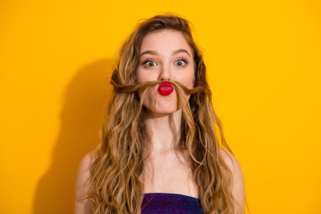 Playful young woman with long blonde hair making a mustache gesture against bright yellow backgroundの写真素材