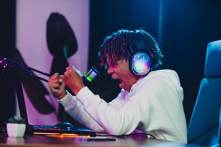 Young gamer enthusiastically streaming a live session with vibrant gear in a modern casual home studio setupの写真素材