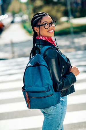 Smiling young woman with a backpack enjoying a sunny day in the city wearing casual style outdoors