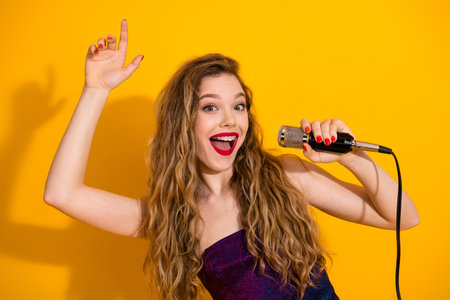 Energetic Young Woman Singing with Joy and Excitement Against a Vibrant Yellow Backgroundの写真素材