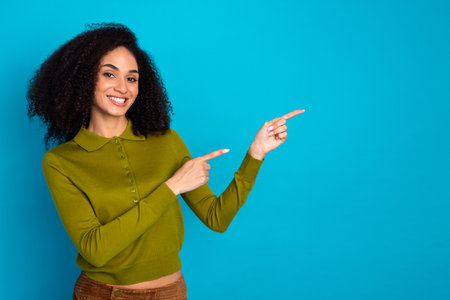 Cheerful young woman in green sweater gesturing over blue background, promoting happiness and positivityの写真素材