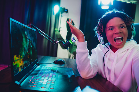 Young gamer streaming online with a laptop and headphones in a neon-lit room showcasing a energetic and fun atmosphereの写真素材