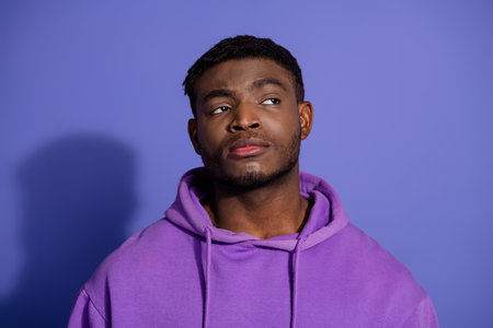 Young male in purple hoodie looking thoughtful against violet background, showcasing casual style and modern fashion.の写真素材