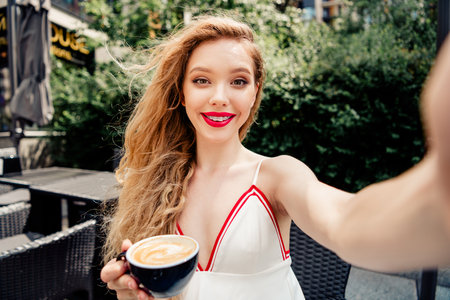 Attractive young woman enjoying coffee outdoors while embracing sunlight in a stylish outdoor cafe