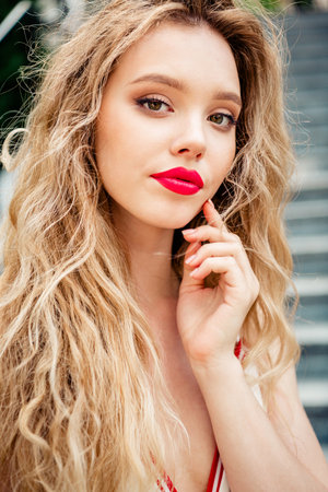 Young woman with glamorous makeup and long blonde hair outdoors in sunlight posing thoughtfully,...