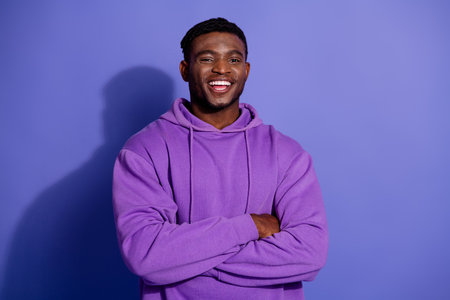Young man in a purple hoodie smiling confidently against a violet background, exuding positivity and casual stylish charmの写真素材