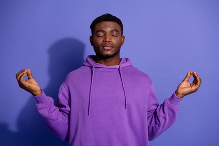 Young african american man practicing meditation, maintaining mental peace while wearing a purple hoodie in a casual styleの写真素材