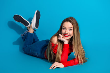 Young woman with long blonde hair in red top posing cheerfully on blue background, conveying modern...