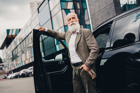 Handsome senior man in a stylish suit exiting his car near a modern city building in an urban daytime settingの写真素材