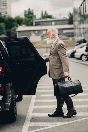 Mature businessman departing by car in an urban setting with a leather bag, demonstrating elegance...