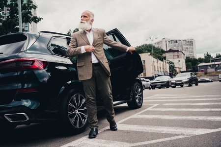 Confident senior gentleman exiting a car amidst an urban street setting showcasing elegant style and professionalismの写真素材