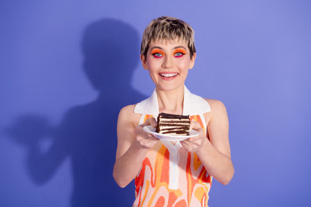 Happy young woman enjoying a piece of chocolate cake on a violet background, exuding positive energy...