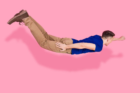 Young Man Posing in a Flying Gesture with His Fist Extended Forward on a Bright Pink Background
