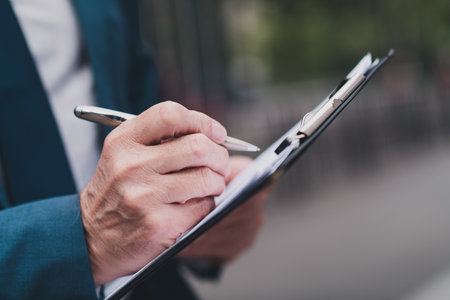 Real estate agent filling out documentation on a clipboard outdoors in an urban environmentの写真素材