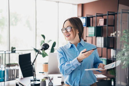 Confident leader sharing insights during office work, holding documents and a pen in a professional business environmentの写真素材