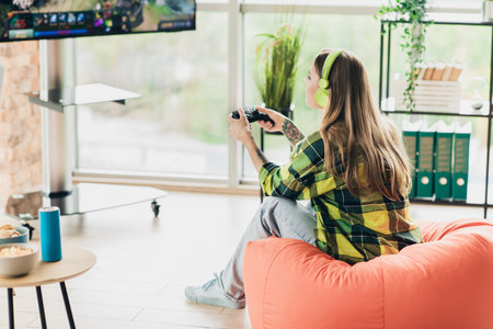 Young woman engaged in modern gaming wearing headphones, working and enjoying leisure time in a...