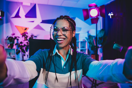 Charming female podcast host recording a media session in a neon-lit creative space, holding a...