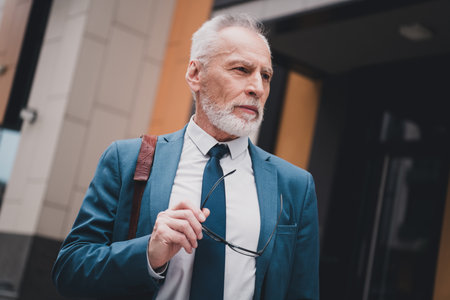 Real estate agency representative in blue suit walking outdoors carrying glasses, embodying professionalism and successの写真素材