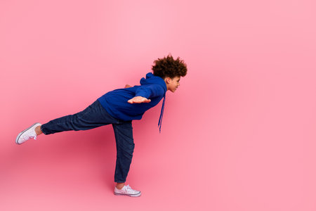 Joyful boy balancing on one foot against a vibrant pink backdrop showcasing vibrant apparel in a...