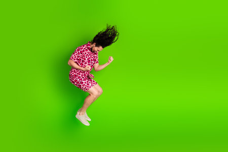 Young man excitedly jumping in a vibrant pink leopard print outfit on a bright green background...