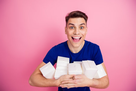 Cheerful young man holding white gift boxes against a pink background showcasing enthusiasm and joy