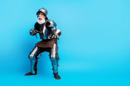 Elderly man in shiny medieval knight armor posing on light blue backgroundの写真素材