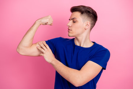 Young man showing his strength by flexing his arm in a confident pose against a light pink backgroundの写真素材