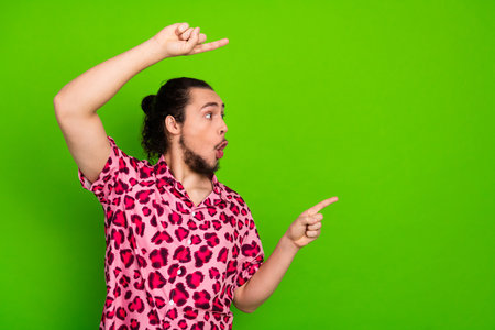 Young man in vibrant pink leopard print shirt gesturing enthusiastically in front of a solid green...