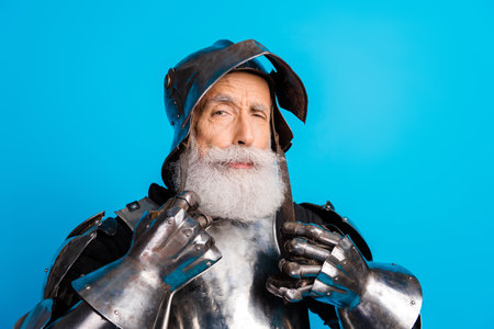 Senior man wearing medieval knight armor posing against a blue background with a confident expressionの写真素材