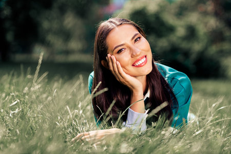 Smiling young woman lying in grass enjoying outdoor leisure in urban park during sunny day