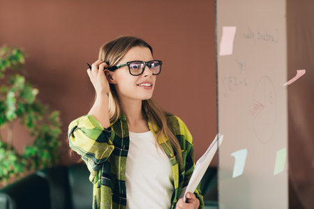Young woman brainstorming ideas on a whiteboard in a business setting for creative professional...