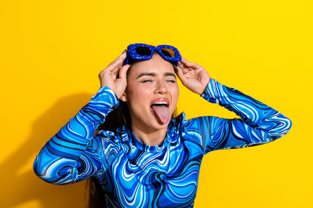 Cheerful Young Woman Posing Playfully in Blue Stylish Top with sunglass Against Bright Yellow Backgroundの写真素材