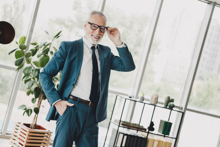 Confident mature businessman posing in formal attire at a modern office, expressing success and professionalismの写真素材