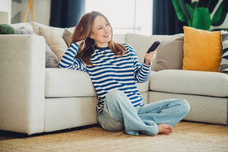 Young woman in casual attire relaxing with a remote control at homeの写真素材