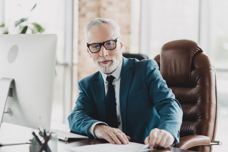 Confident senior businessman working at his office desk in a corporate environment with a computer and documentsの写真素材