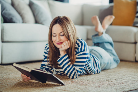 Young woman reading a book in a cozy home setting wearing a striped casual sweatshirt, relaxing indoors on the weekend.の写真素材