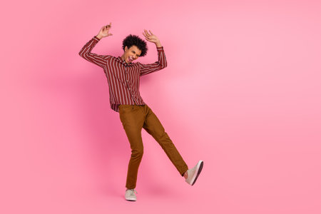 Cheerful man with curly hair joyfully dancing on a pink background wearing stylish casual attire and brown pantsの写真素材