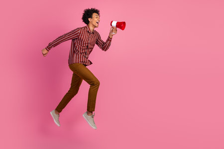 Cheerful man cheerfully jumping holding a megaphone against a bright pink background conveying enthusiasm and styleの写真素材