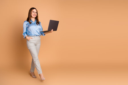 Confident Businesswoman Holding Laptop on Beige Background Depicting Professionalism and Elegance in Formal Attireの写真素材