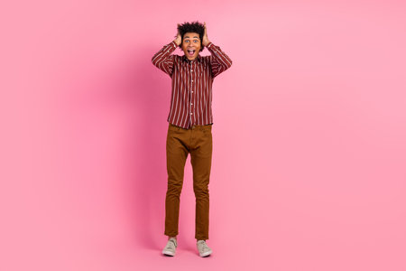 Excited young man in striped shirt and casual attire expressing joy against a pink studio backgroundの写真素材